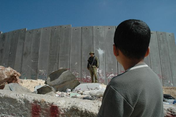 Niño palestino observa a un soldado israelí frente al muro del apartheid