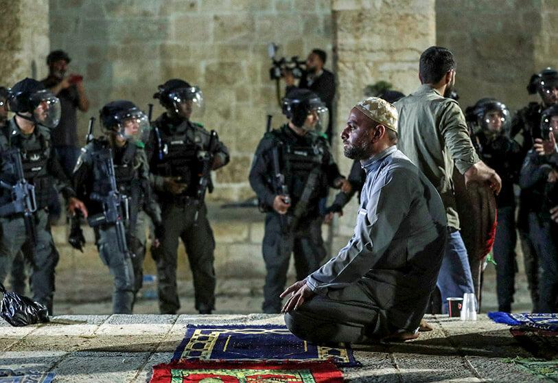 Palestino musulmán rezando con un equipo antidisturbios israelí de fondo