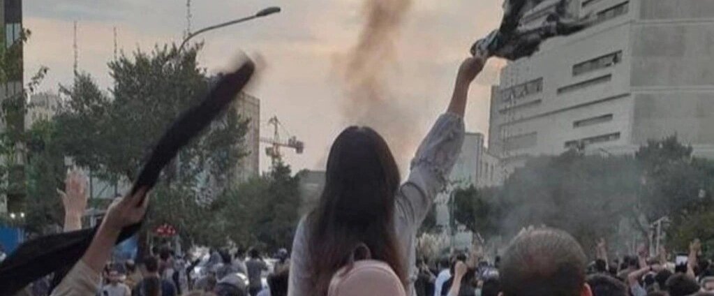 Una mujer en una protesta en Irán alza un velo con la mano.