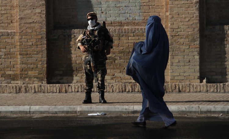 Un oficial de seguridad afgano armado monta guardia mientras una mujer con burka camina cerca de en una mezquita, en Herat, Afganistán. EFE/EPA/JALIL REZAYEE