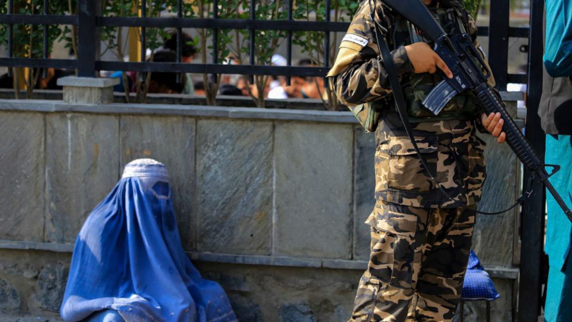 Una mujer afgana vestida con burka pide limosna mientras los talibanes hacen guardia en un lugar público en Kabul, Afganistán, el 27 de julio de 2022. EFE/EPA/STRINGER