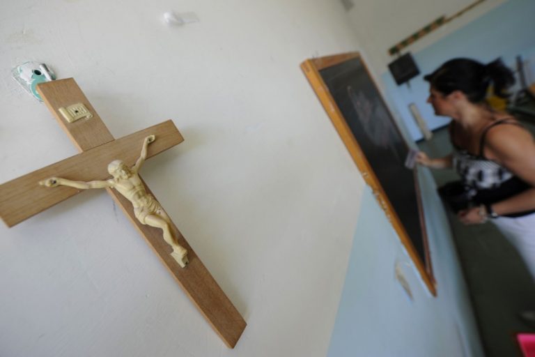 Un crucifijo cuelga en la pared de un aula en el que una profesora escribe en la pizarra. /AFP