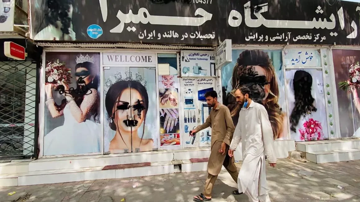 Dos hombres caminan junto a un salón de belleza cerrado y vandalizado en una calle de Kabul, Afganistán. EFE / Stringer