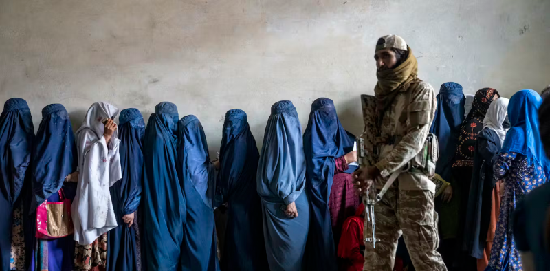 Un combatiente talibán monta guardia mientras unas mujeres esperan para recibir raciones de comida distribuidas por un grupo de ayuda humanitaria, en Kabul, Afganistán, en mayo de 2023. (AP Photo/Ebrahim Noroozi, File)