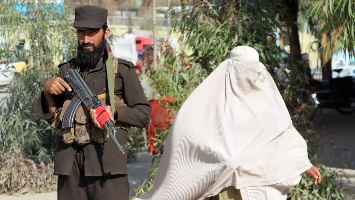 Una mujer vestida con burka pasa mientras los talibanes afganos vigilan a personas y vehículos en un puesto de control, en Kandahar, Afganistán, 18 de marzo de 2024 EFE/EPA/QUDRATULLAH RAZWAN