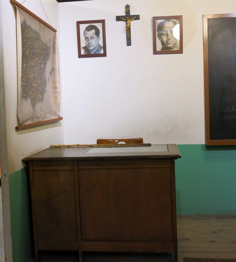 Recreación de un aula típica de una escuela durante el franquismo, presidida por un crucifijo y los retratos de Franco (a su derecha) y de José Antonio Primo de Rivera (a su izquierda). Museu d'Història de Catalunya. Foto: Wikipedia