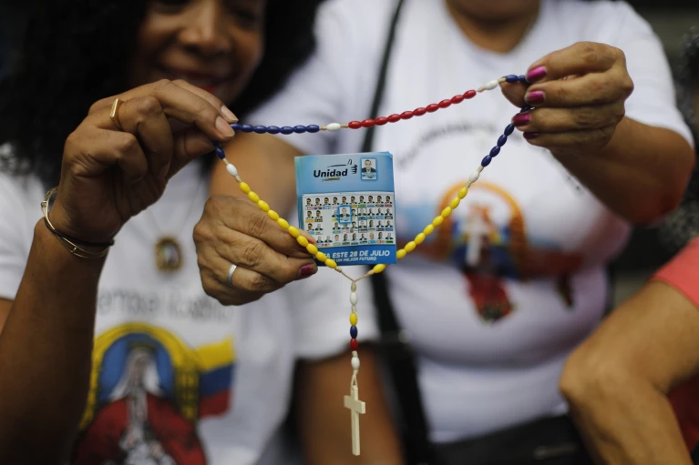 Partidarios de la oposición sostienen un rosario con un volante que muestra al candidato presidencial Edmundo González durante un evento de oración en Caracas, Venezuela, el domingo 21 de julio de 2024. Venezuela celebrará elecciones presidenciales el 28 de julio. (AP Foto/Cristian Hernandez)