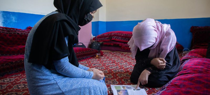 © UNICEF/Amin Meerzad Una mujer afgana ayuda a su hermana pequeña a estudiar en su casa.